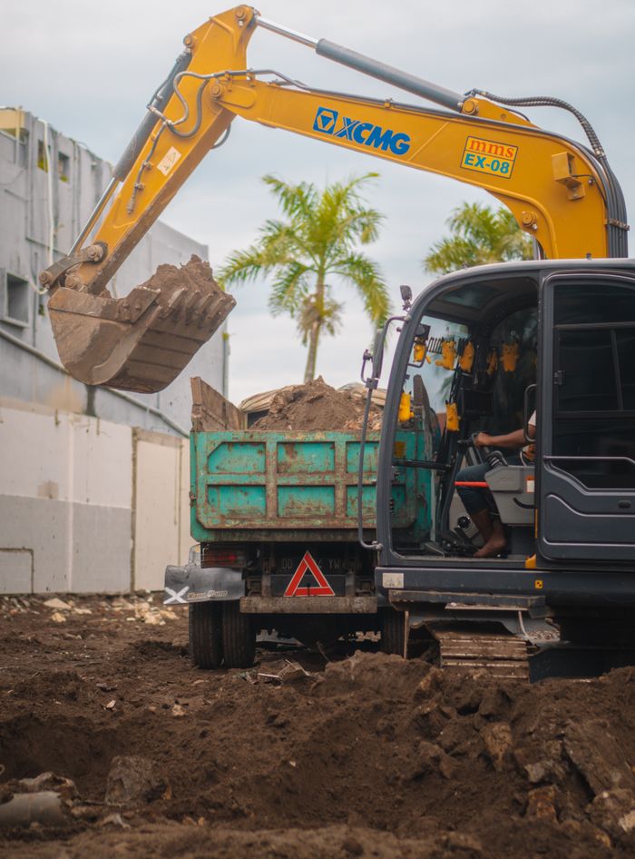 Excavator loading dirt into a truck at a construction site in Makassar, Indonesia.